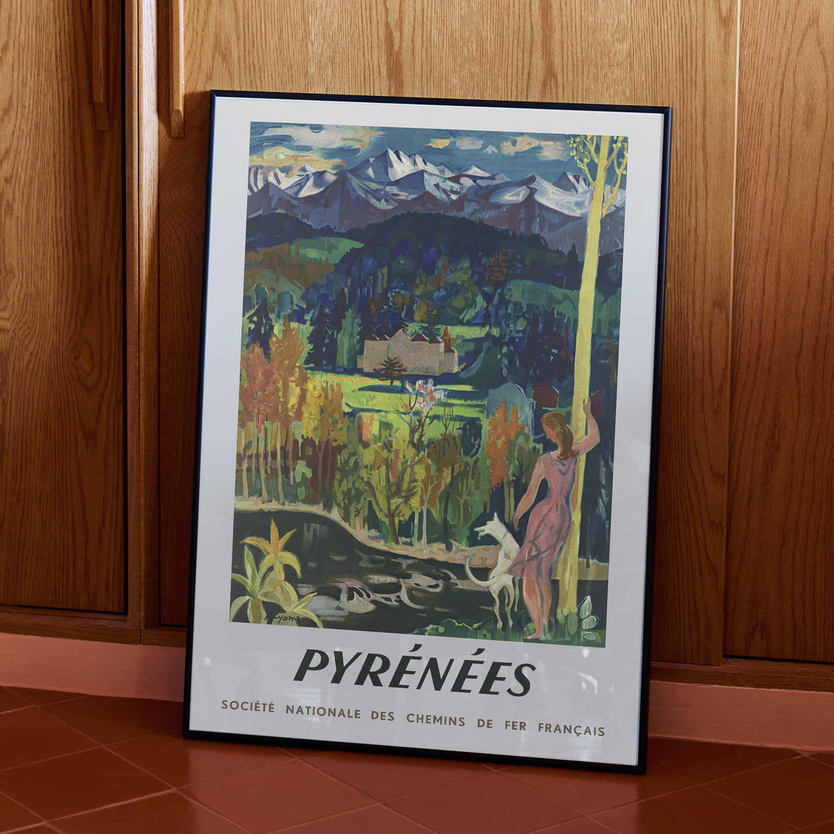 Pyrenees Railway poster by Roger Aujame with alpine peaks, green valley, blue skies, and woman by stream, framed and displayed in modern living room decor