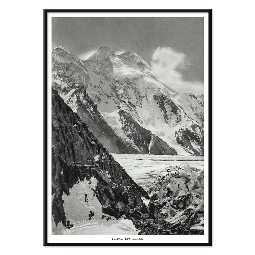 Black and white photograph and poster of Broad Peak by Vittorio Sella showing snow covered mountains and mountaineers climbing amidst rocky terrain and glacier, with black aluminium frame on white background