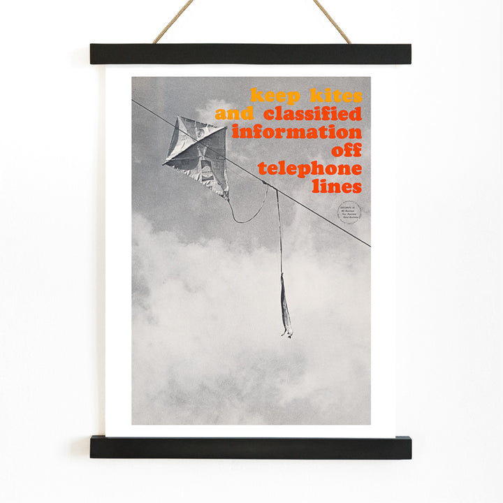 Black and white photo and poster of a kite tangled on a telephone line with bold warning text Keep kites and classified information off telephone lines, with wooden magnetic frame on white background