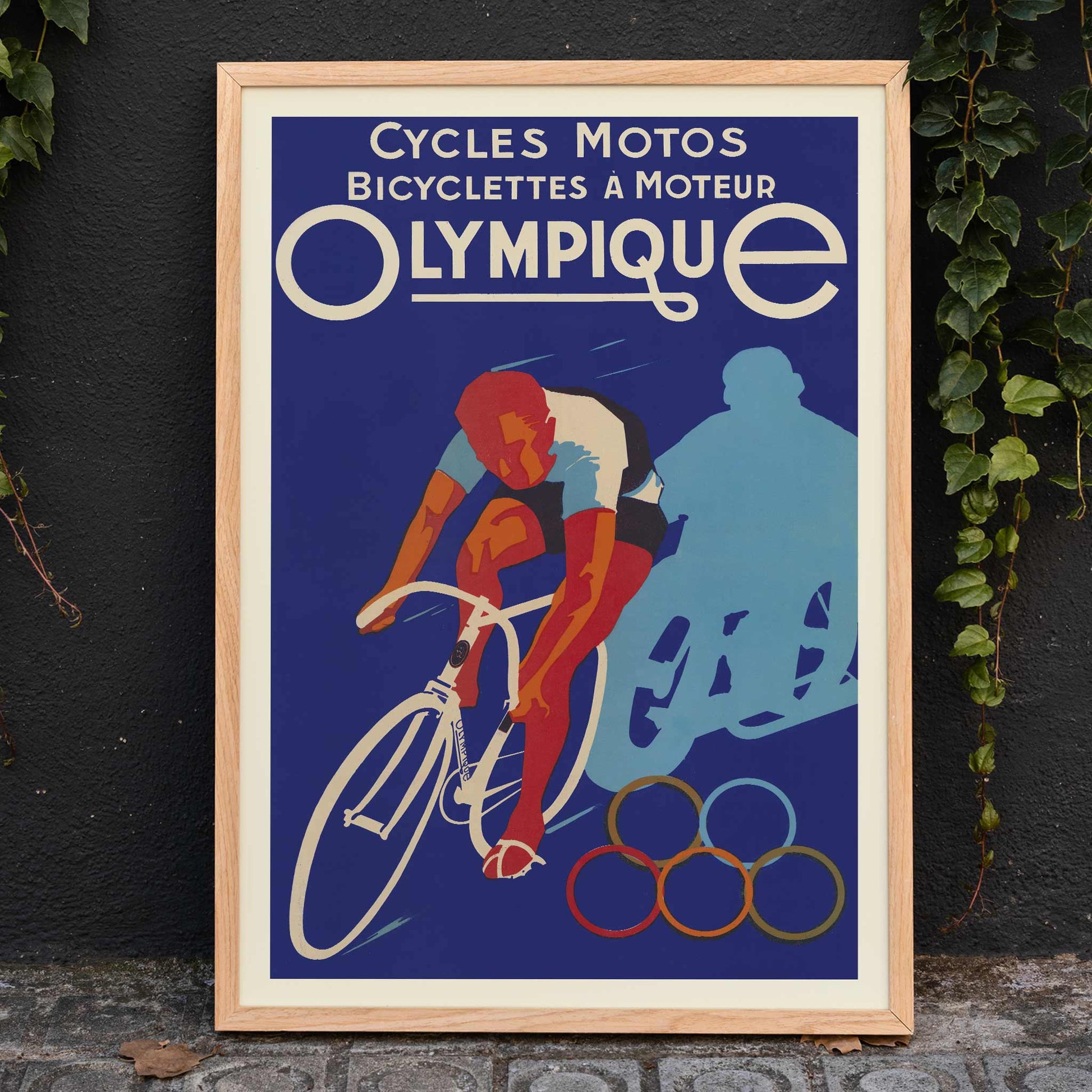 Affiches Gaillard Cycles olympique poster featuring a racing cyclist, bold lettering, blue background, and Olympic rings in vintage style, framed and displayed in modern living room decor