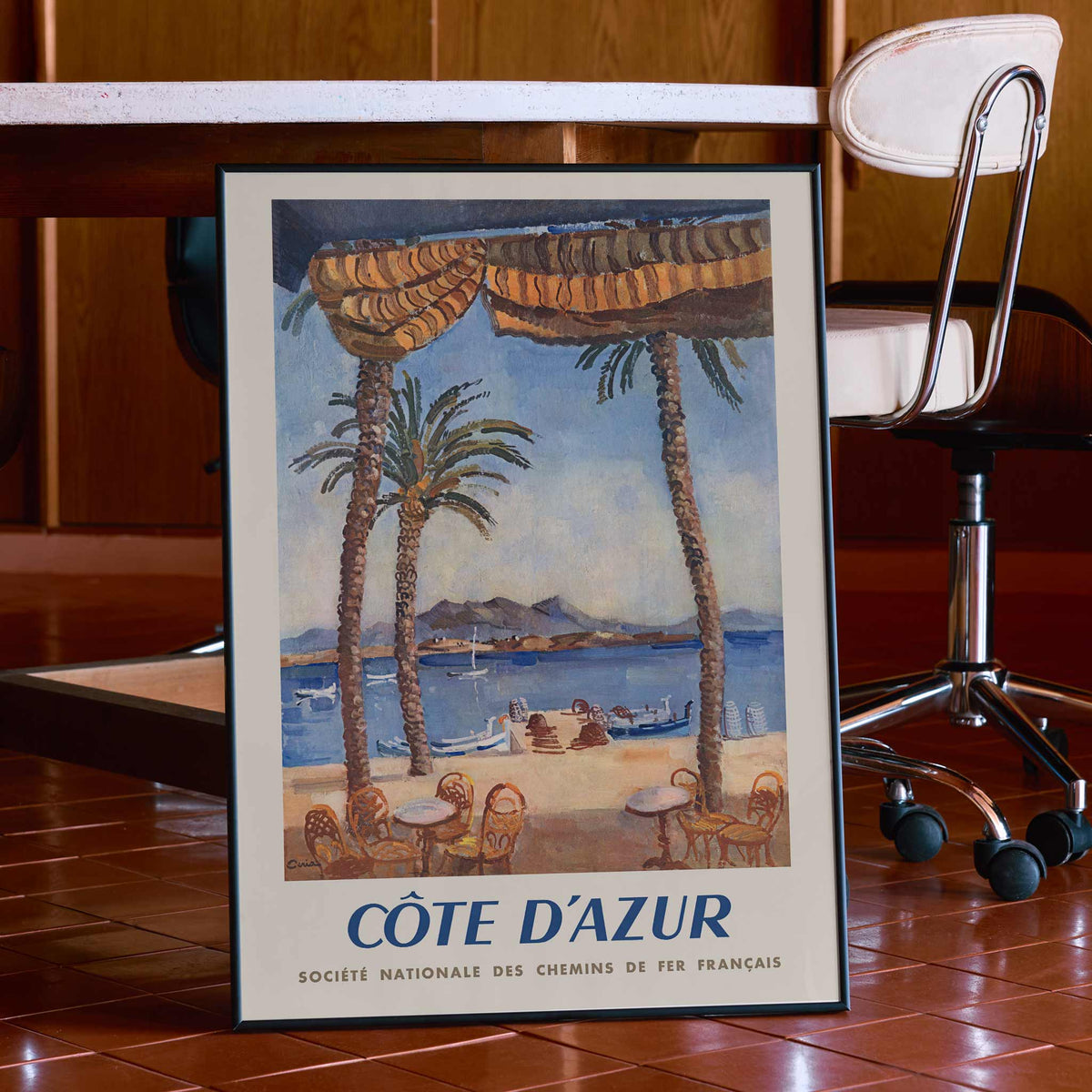 Edmond Céria French Riviera Railway poster with palm trees, blue sea, sandy beach, ochre canopies, vintage travel style, framed and displayed in modern living room decor