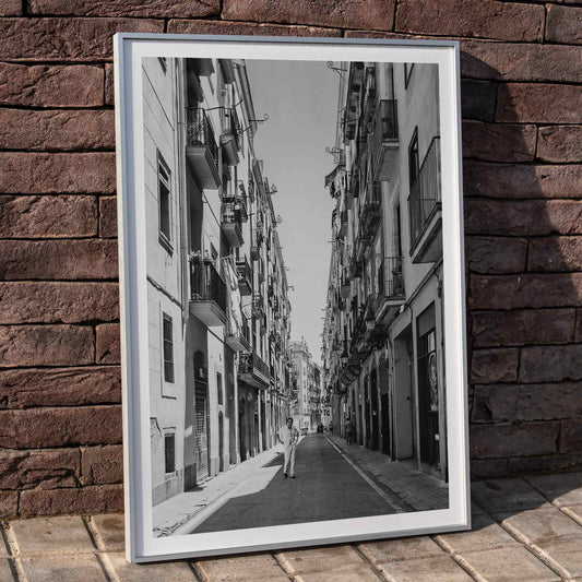 Black and white photo poster of a narrow street in Barcelona featuring a person walking in the center perfect for urban wall art, framed and displayed in home decor