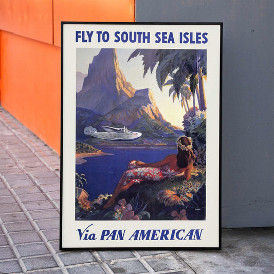 Vintage travel poster of a woman in a floral dress on a tropical island with a Pan American seaplane by Paul George Lawler, framed and displayed in home decor