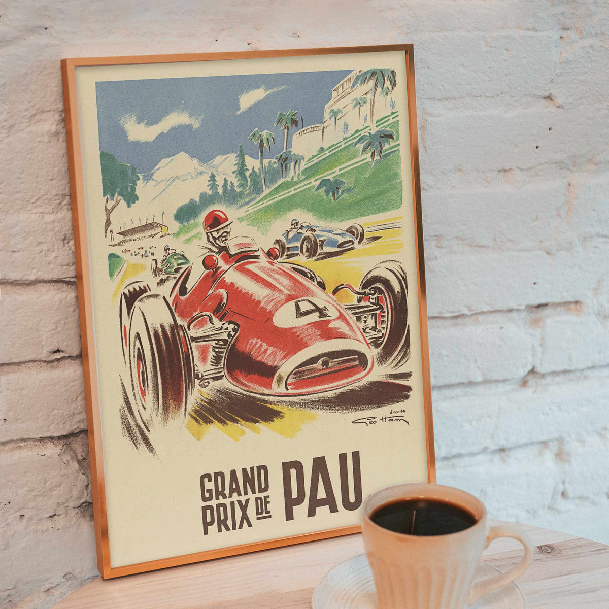 Georges Hamel Grand Prix de Pau poster with red racing car on a sunlit circuit near green hills and mountain castle, framed and displayed in modern living room decor